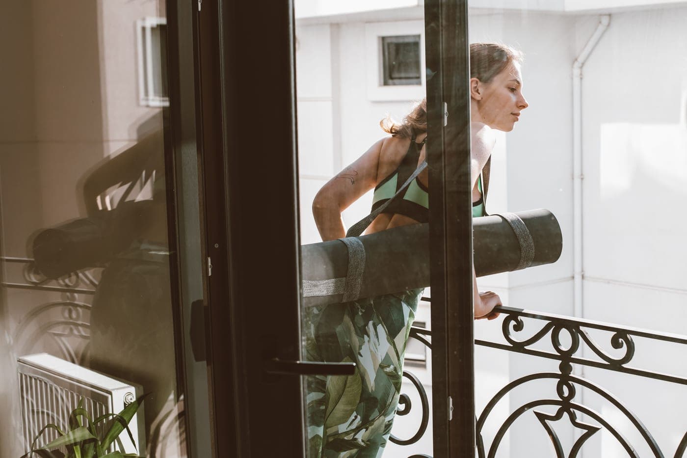 Someone in sportswear resting on a balcony beside a mat