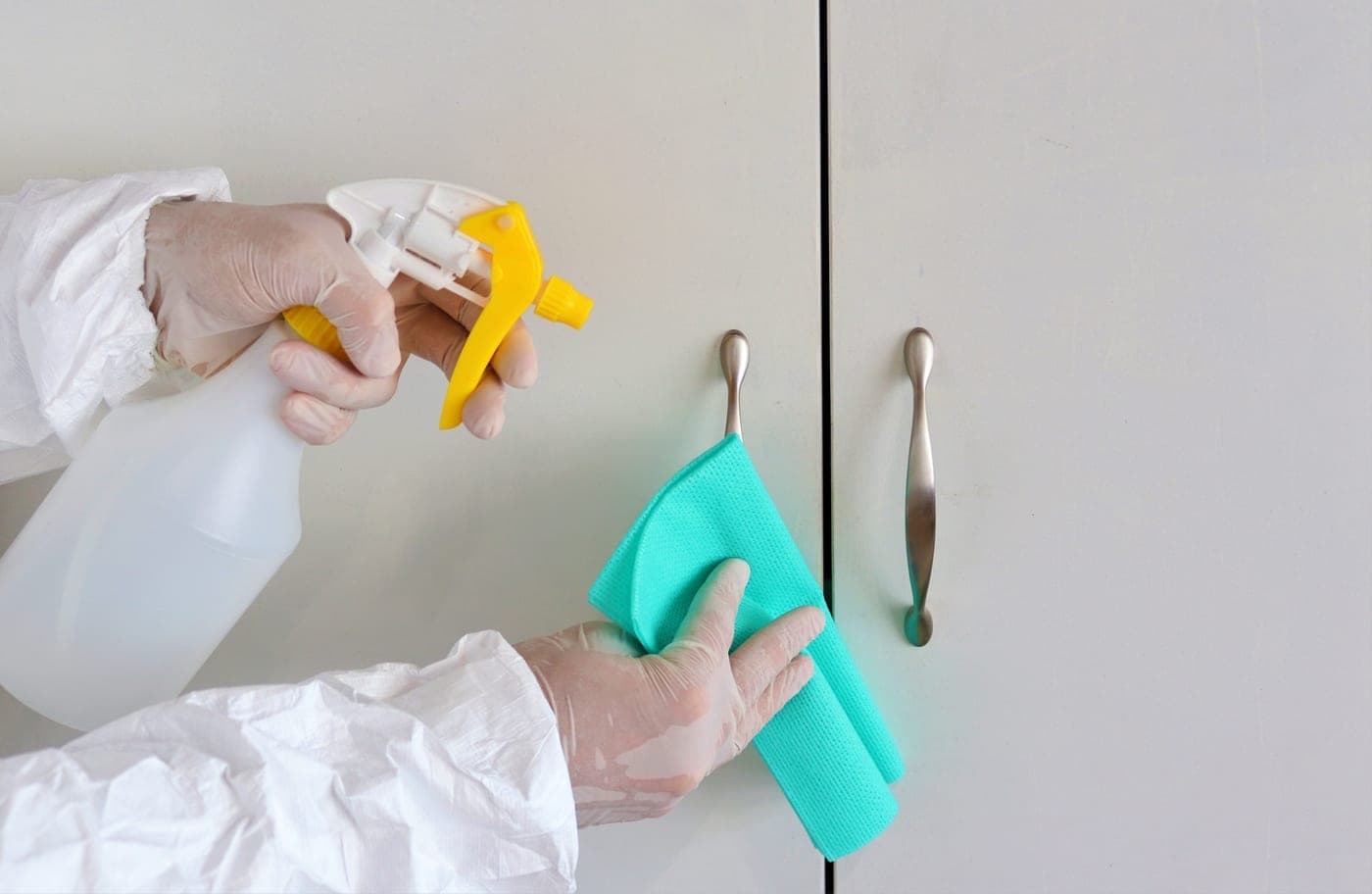 Gloved hands wiping a surface with a cloth and spray bottle
