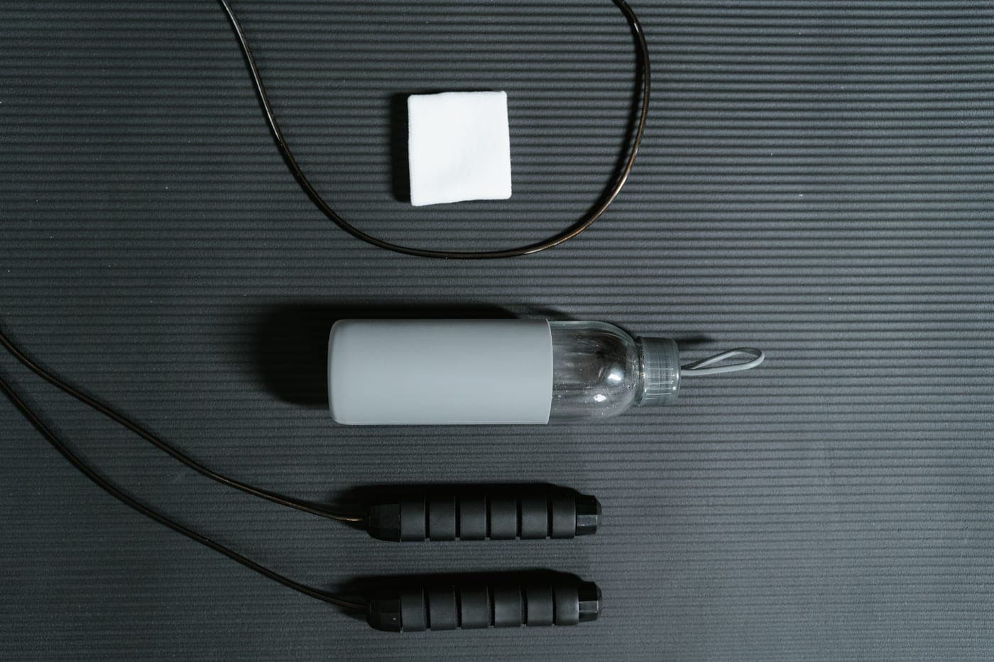 A towel, water bottle and jump rope laid on an exercise mat