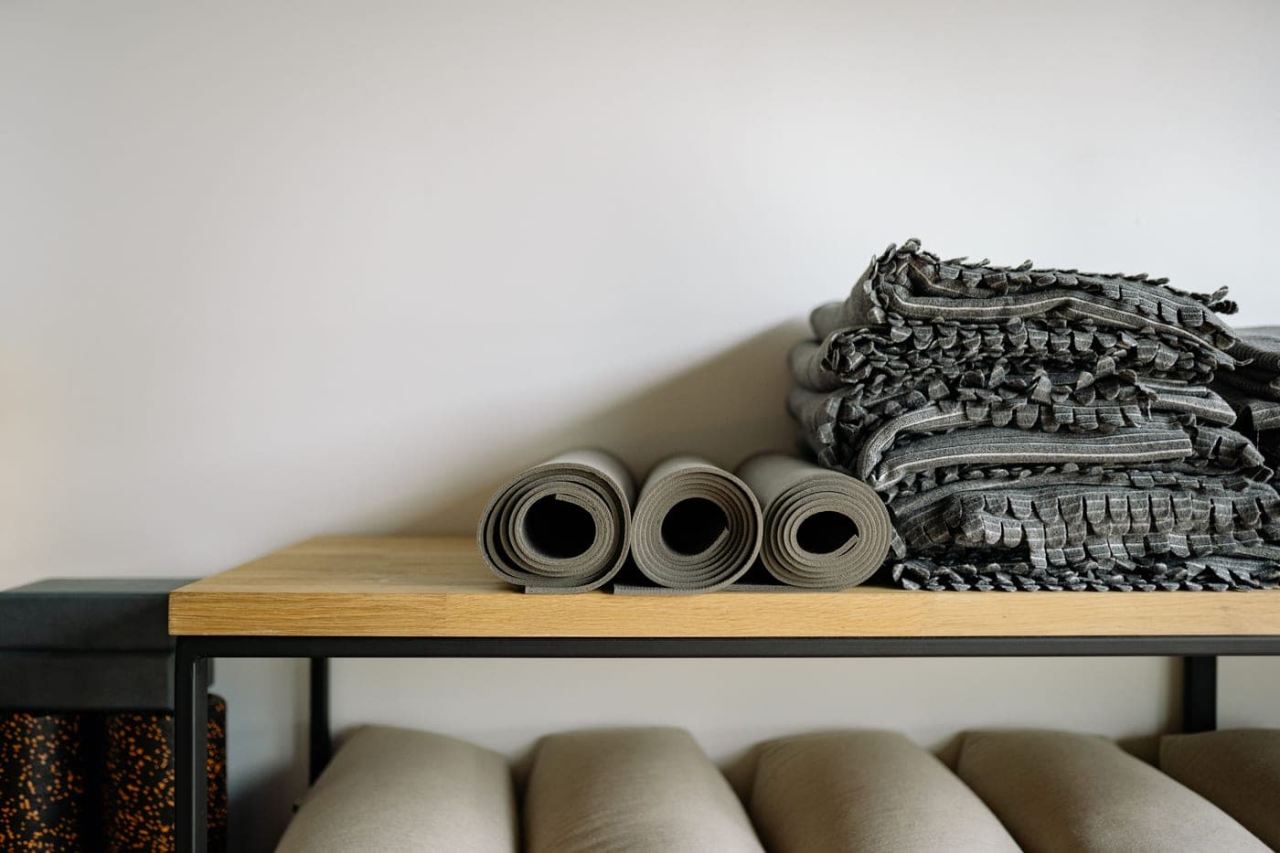 Rolled mats and folded blankets stored on a studio shelf