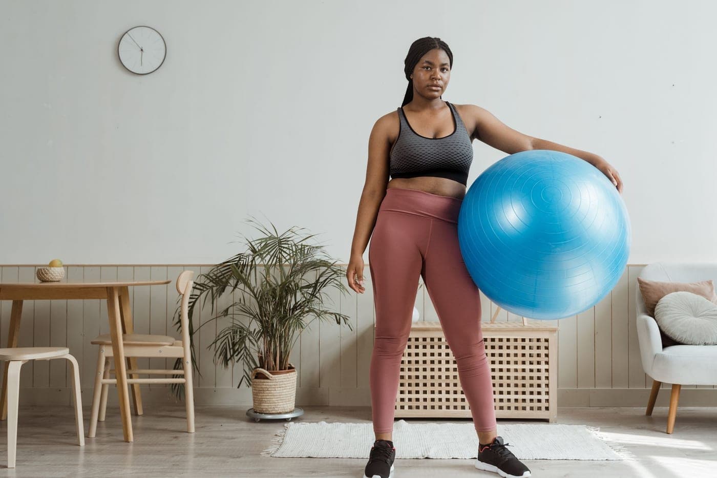 Someone in activewear standing beside a large exercise ball in a bright living room