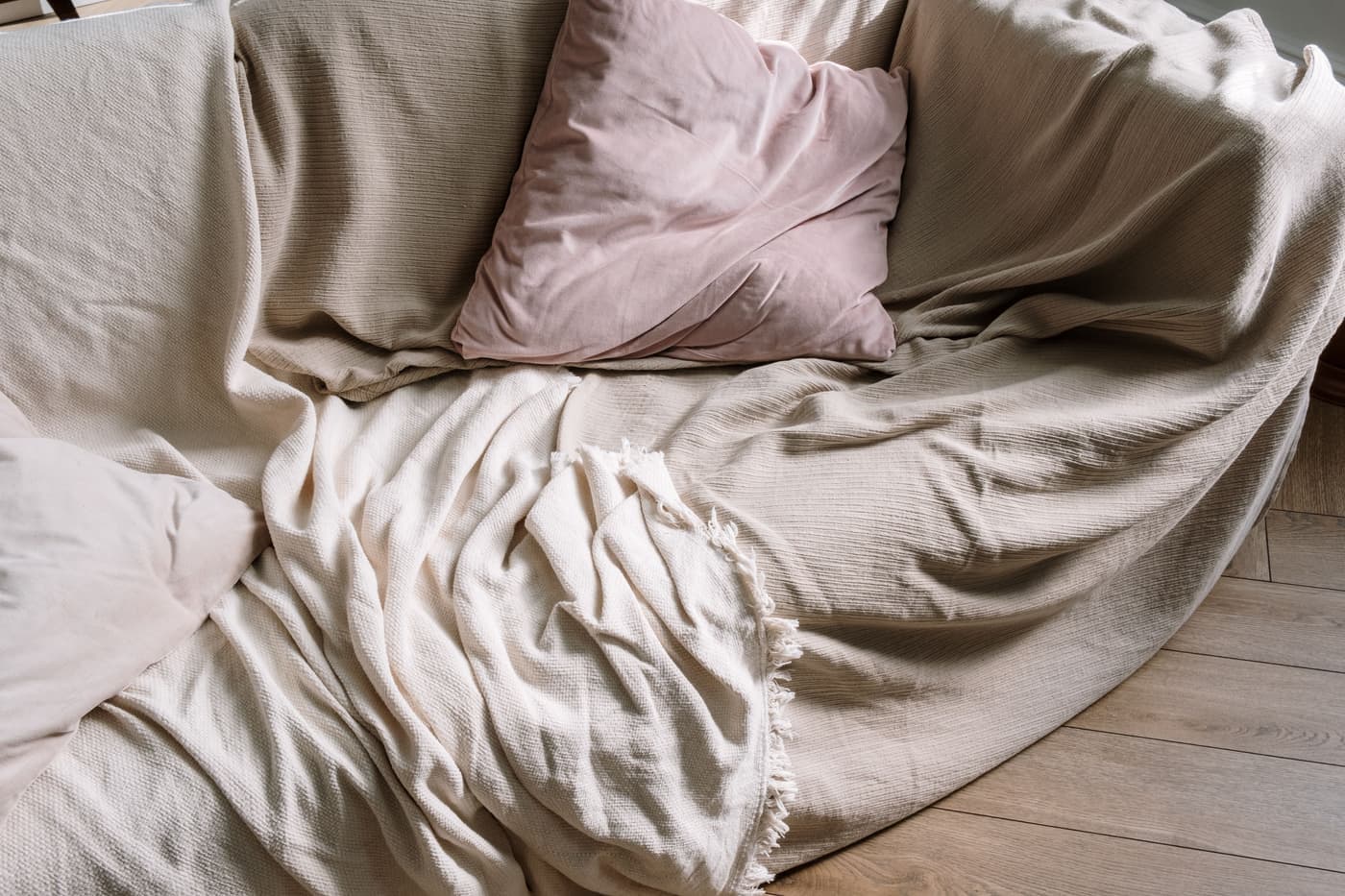 A sofa with plush cushions and a blanket over a wooden floor