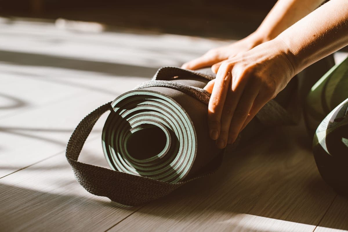 Stock photo: close-up of hands rolling up a mat on a sunlit hardwood floor