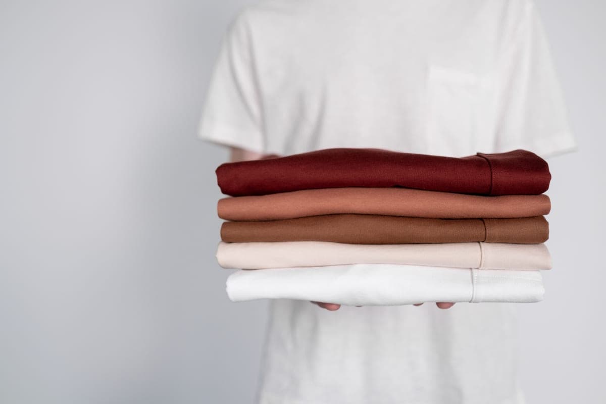 Stock photo: hands holding a stack of neatly folded tops in earthy tones